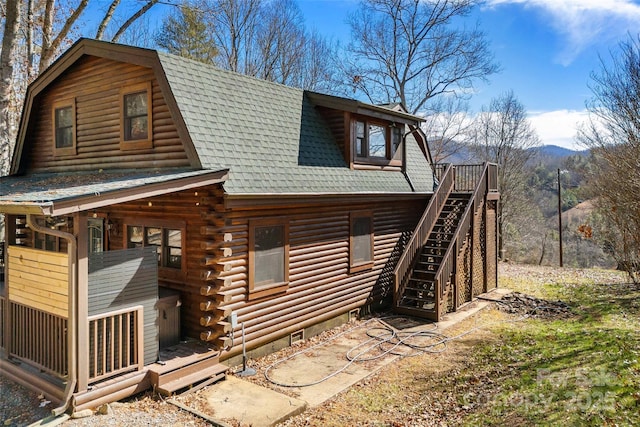 view of home's exterior featuring a shingled roof, stairway, a gambrel roof, log exterior, and a wooden deck