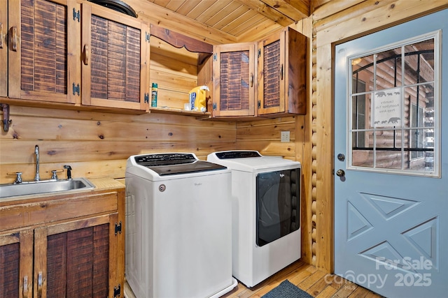 clothes washing area with cabinet space, independent washer and dryer, wooden walls, and a sink