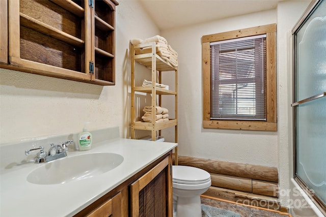 bathroom with enclosed tub / shower combo, a textured wall, vanity, and toilet