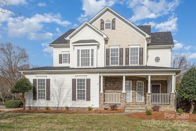 view of front of house featuring stone siding, a front yard, and covered porch