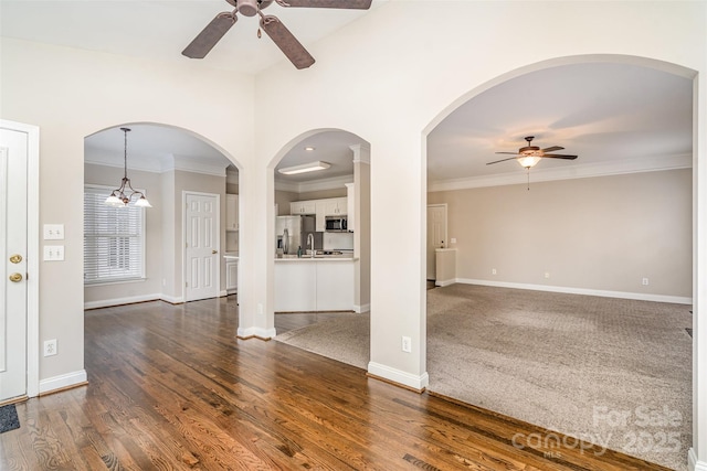 unfurnished living room featuring baseboards, ceiling fan, dark wood-style flooring, and crown molding