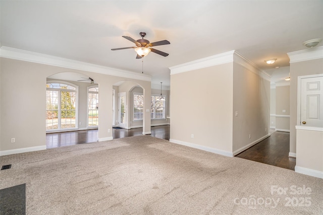 unfurnished living room featuring arched walkways, ornamental molding, dark carpet, and a ceiling fan