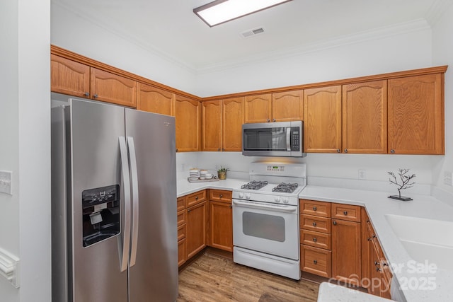 kitchen featuring hardwood / wood-style floors, stainless steel appliances, ornamental molding, and sink