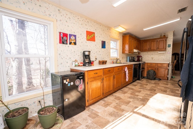 kitchen with light countertops, range with two ovens, freestanding refrigerator, and wallpapered walls