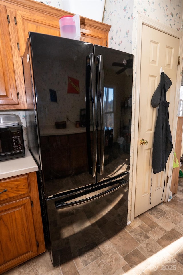 kitchen with light countertops, brown cabinetry, stone finish floor, black appliances, and wallpapered walls