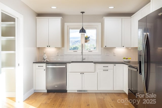 kitchen with stainless steel appliances, light wood finished floors, dark countertops, and white cabinets