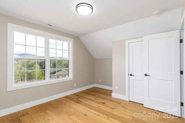 additional living space with light wood-style flooring, visible vents, baseboards, and vaulted ceiling