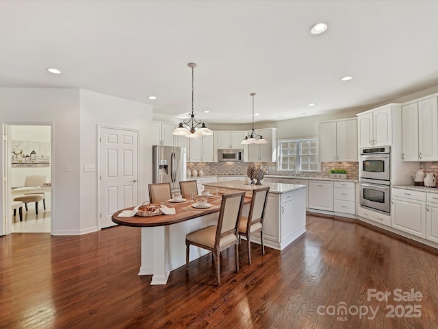 kitchen featuring white cabinetry, light stone counters, a center island, pendant lighting, and stainless steel appliances