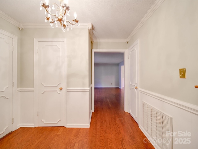 corridor with crown molding, hardwood / wood-style floors, and an inviting chandelier