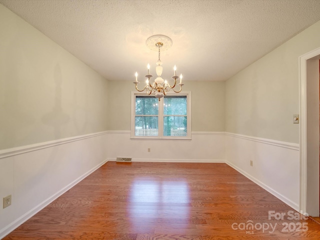 spare room featuring a chandelier, hardwood / wood-style floors, and a textured ceiling