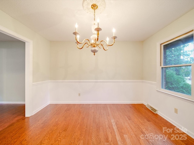 spare room with hardwood / wood-style flooring, an inviting chandelier, and a textured ceiling