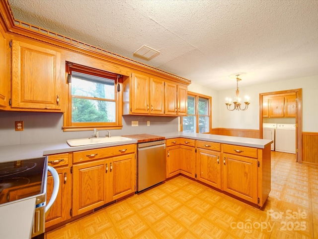 kitchen with decorative light fixtures, sink, stainless steel dishwasher, washing machine and clothes dryer, and kitchen peninsula