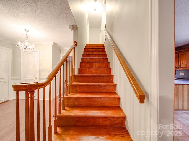 stairs featuring a notable chandelier, wood-type flooring, ornamental molding, and a textured ceiling