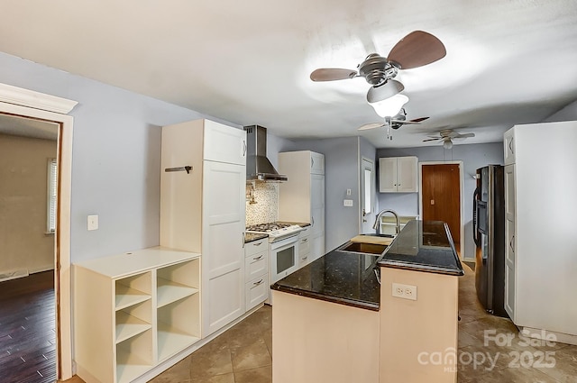 kitchen with sink, white cabinetry, tasteful backsplash, an island with sink, and wall chimney range hood