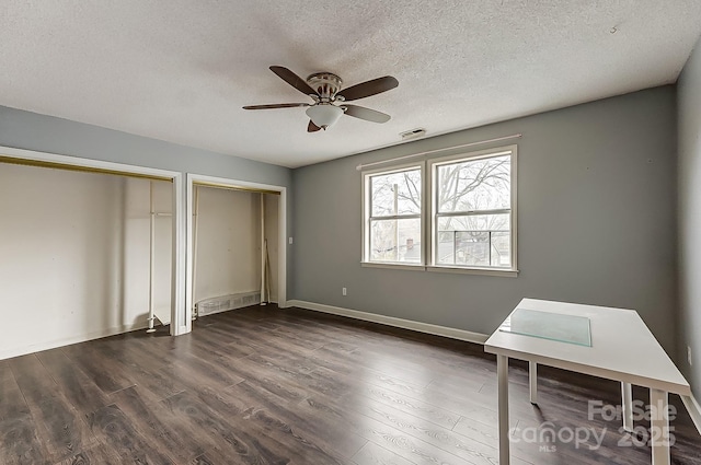 unfurnished bedroom featuring dark hardwood / wood-style flooring, ceiling fan, two closets, and a textured ceiling