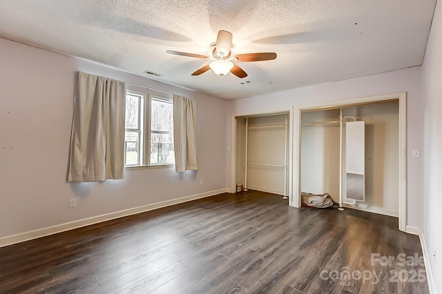 unfurnished bedroom featuring ceiling fan, dark hardwood / wood-style floors, two closets, and a textured ceiling