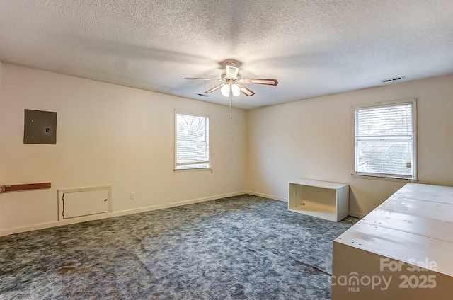 unfurnished office featuring ceiling fan, a textured ceiling, electric panel, and dark carpet