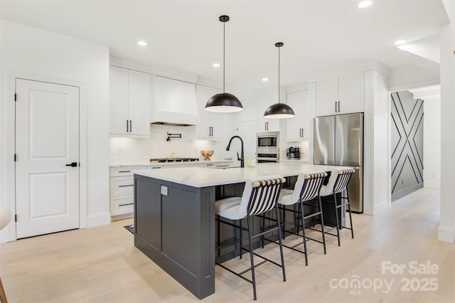 kitchen with a large island, stainless steel appliances, light countertops, hanging light fixtures, and white cabinets