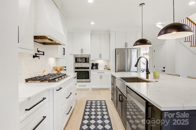 kitchen featuring stainless steel appliances, premium range hood, white cabinetry, a center island with sink, and pendant lighting