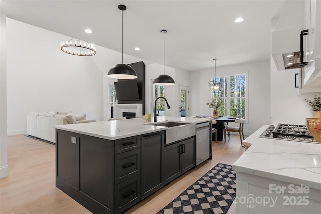 kitchen featuring open floor plan, appliances with stainless steel finishes, light stone countertops, an island with sink, and pendant lighting