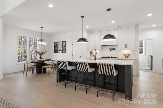 kitchen featuring a spacious island, white cabinetry, light wood-type flooring, backsplash, and decorative light fixtures