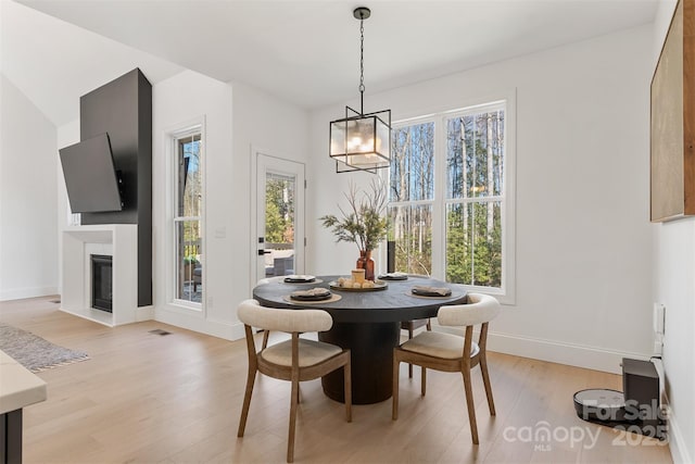 dining space with a fireplace with flush hearth, baseboards, plenty of natural light, and light wood finished floors