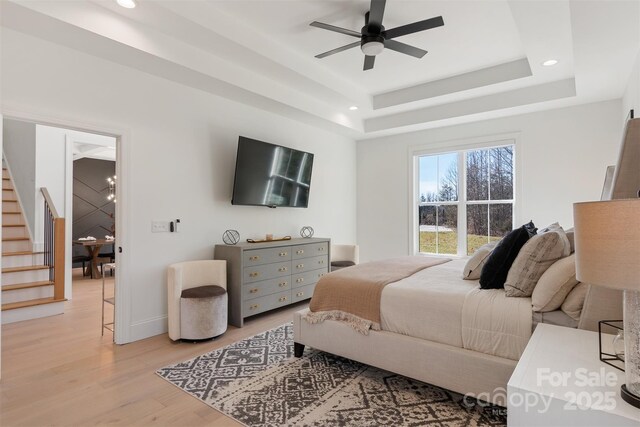 bedroom with a tray ceiling, a notable chandelier, light wood finished floors, recessed lighting, and baseboards