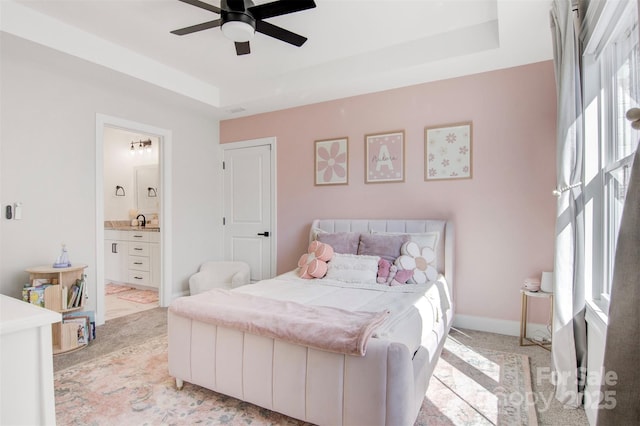 bedroom with light carpet, a sink, baseboards, a tray ceiling, and ensuite bath