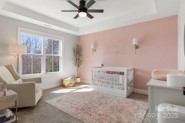 bedroom featuring carpet floors, a tray ceiling, a crib, and baseboards