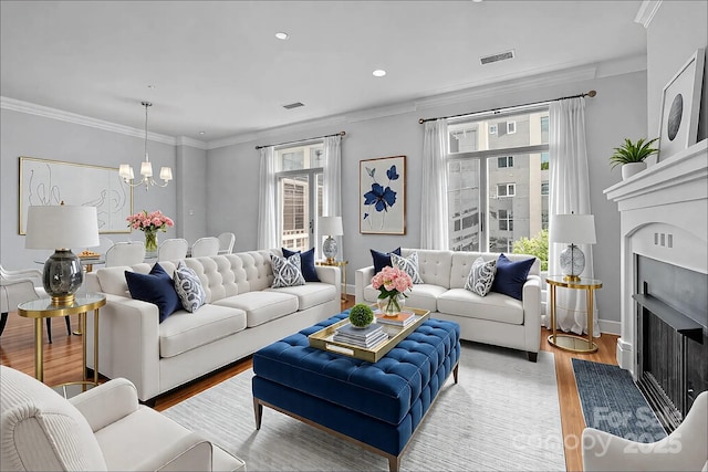 living area with light wood finished floors, visible vents, a chandelier, ornamental molding, and a fireplace