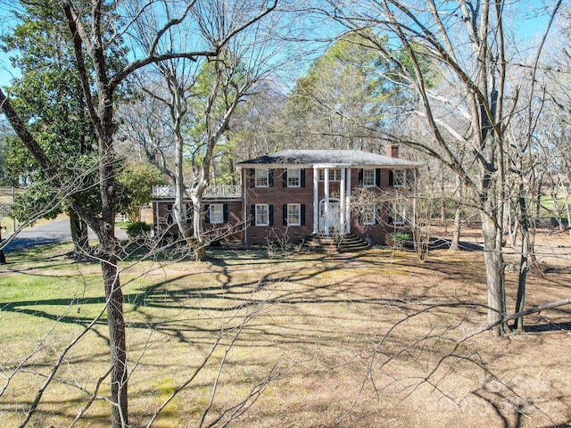 greek revival house featuring brick siding, a chimney, and a front yard