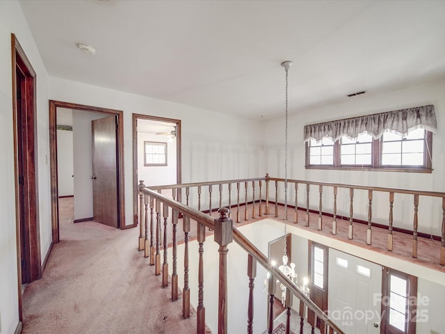 hallway featuring visible vents, light colored carpet, and an upstairs landing