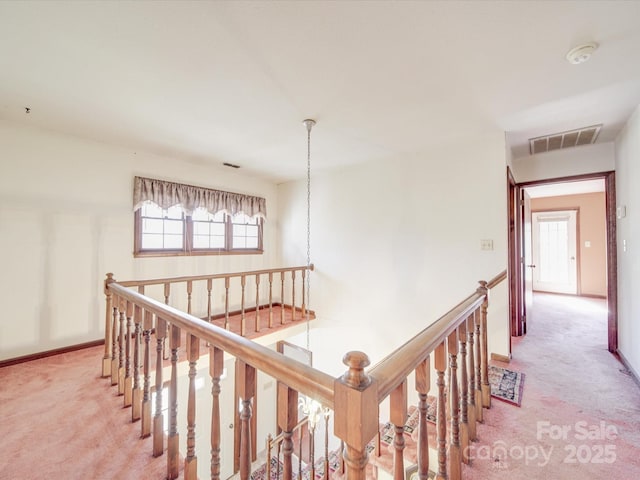 hall featuring carpet floors, baseboards, visible vents, and an upstairs landing