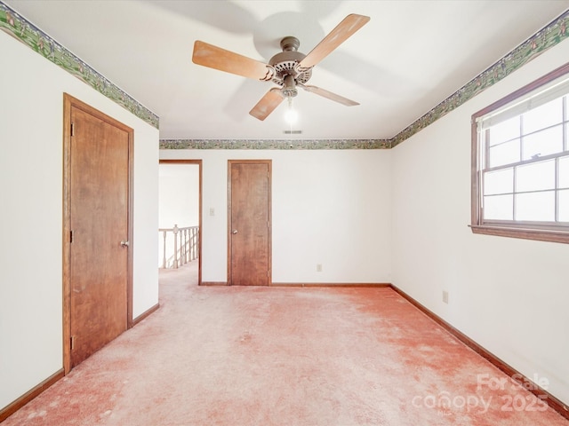 empty room with baseboards, visible vents, ceiling fan, and light colored carpet