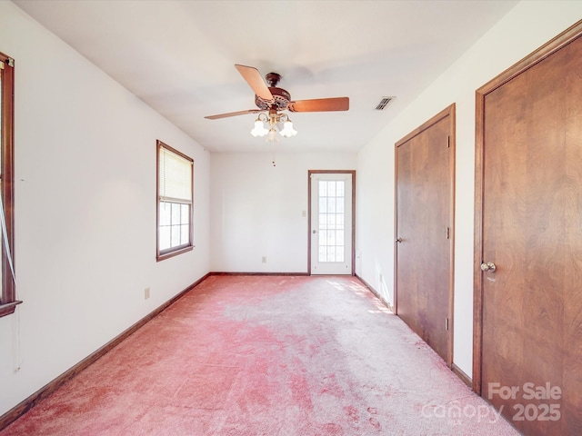 empty room featuring light carpet, ceiling fan, visible vents, and baseboards