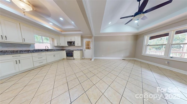 kitchen featuring sink, dark stone countertops, backsplash, stainless steel appliances, and a raised ceiling