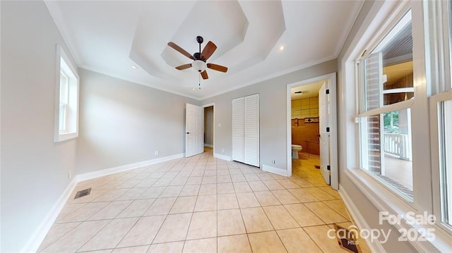 unfurnished bedroom with light tile patterned floors, ceiling fan, ensuite bathroom, ornamental molding, and a raised ceiling