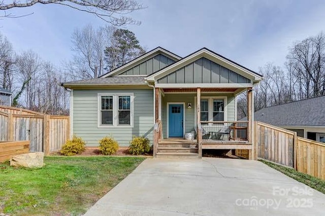 view of front of home featuring board and batten siding, covered porch, fence, and a front lawn