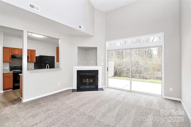 unfurnished living room with visible vents, baseboards, a fireplace with flush hearth, dark colored carpet, and high vaulted ceiling