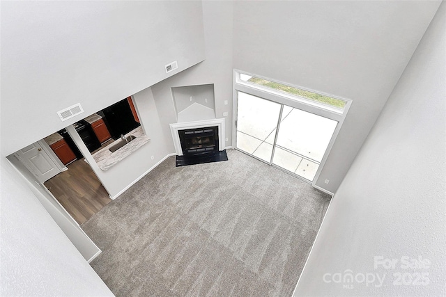 unfurnished living room with carpet floors, a fireplace, a towering ceiling, and visible vents