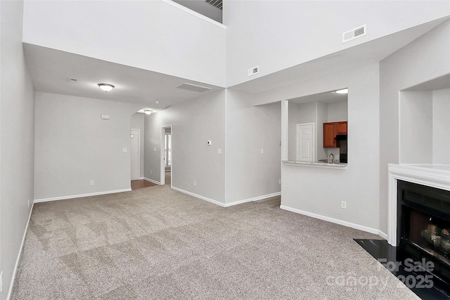 unfurnished living room with baseboards, a fireplace with flush hearth, visible vents, and carpet flooring