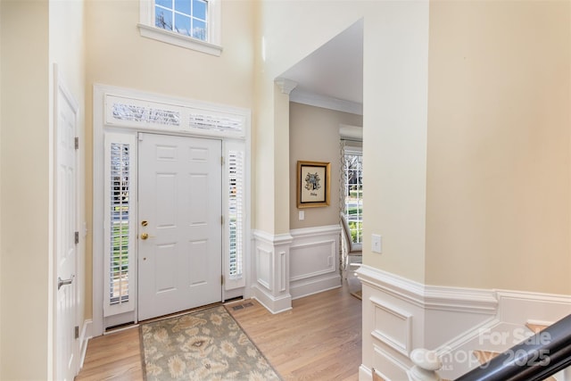 foyer entrance with ornate columns, ornamental molding, and light hardwood / wood-style flooring