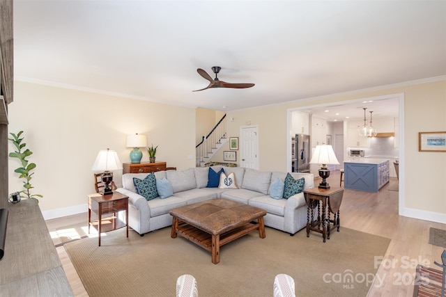 living room with light hardwood / wood-style flooring, ornamental molding, and ceiling fan with notable chandelier