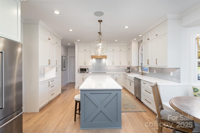 kitchen featuring hanging light fixtures, appliances with stainless steel finishes, a kitchen island, light wood-type flooring, and white cabinets