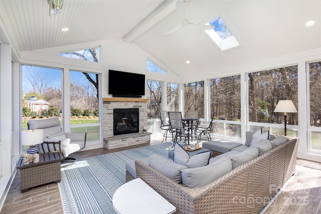 sunroom / solarium featuring lofted ceiling with skylight, ceiling fan, and an outdoor stone fireplace