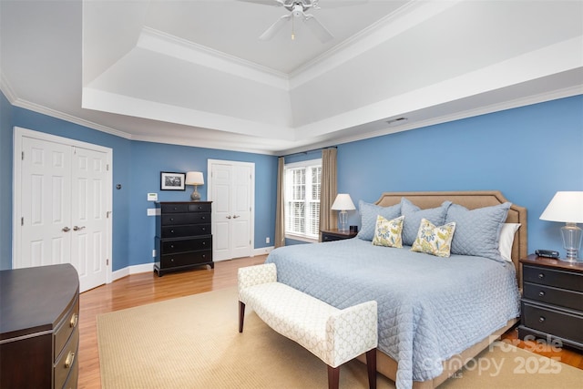 bedroom with a tray ceiling, crown molding, two closets, and wood-type flooring