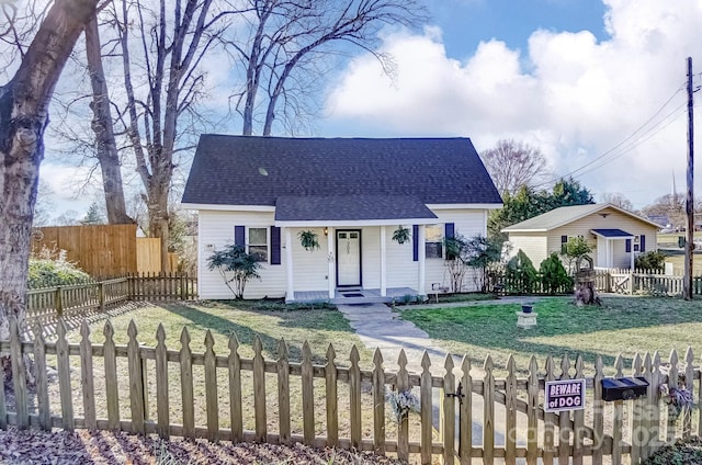 view of front of home with a shingled roof, a porch, a fenced front yard, and a front lawn