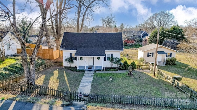 view of front of property with a fenced front yard, a front yard, roof with shingles, and an outdoor structure