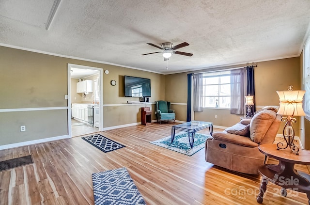 living room featuring crown molding, visible vents, light wood-style floors, ceiling fan, and a textured ceiling