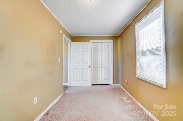 unfurnished bedroom with carpet, a closet, visible vents, ornamental molding, and baseboards